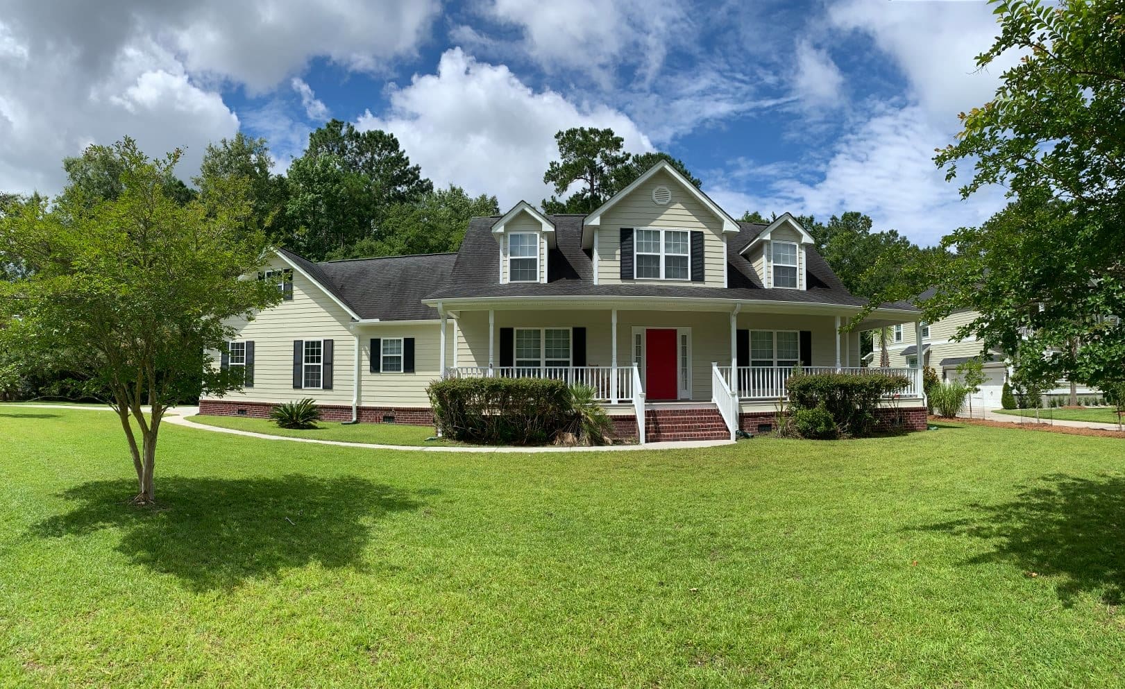 A large white house with red door and green grass.