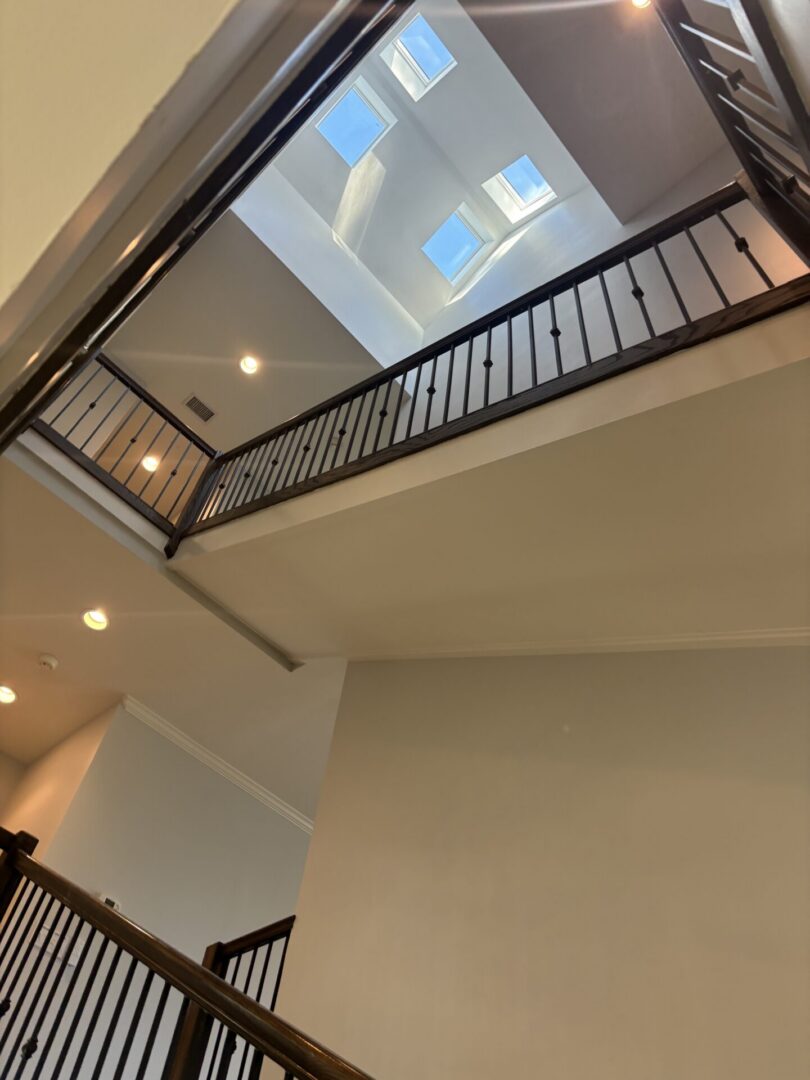Freshly painted multi-story foyer with tall walls, dark wood railings, recessed lighting, and a skylight feature.